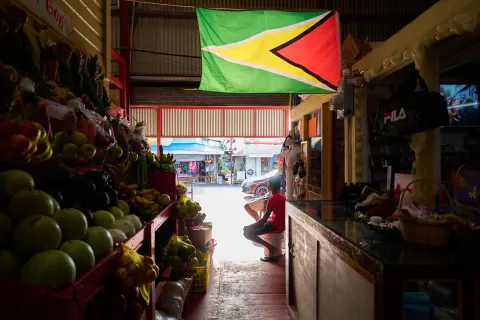 A Guyanese flag hanging above fruit stalls in a covered market.