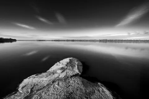 A black-and-white river landscape with a large rock in the foreground.