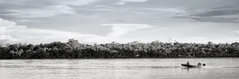 A monochrome view of a small boat on a wide river beneath clouds.