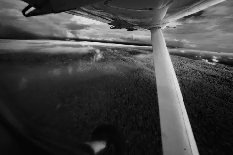 A black-and-white view past an aircraft strut over water and forest.