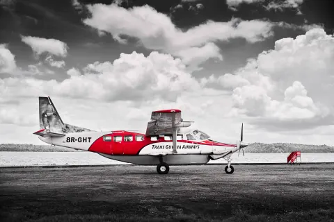 A red and white propeller aircraft on a runway, with the surroundings in monochrome.