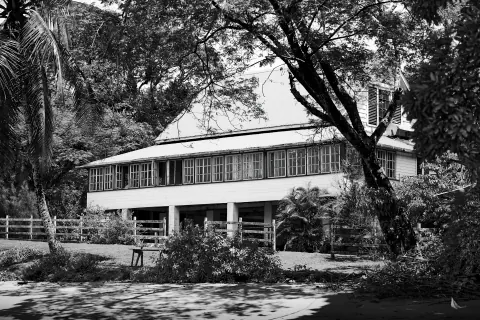 A black-and-white photograph of a two-storey building among large trees.