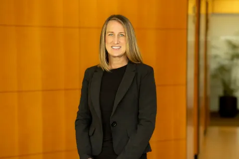 A smiling woman in a black blazer beside a wood-panelled office wall.