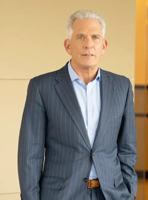 A grey-haired man in a striped suit and open-collar shirt.