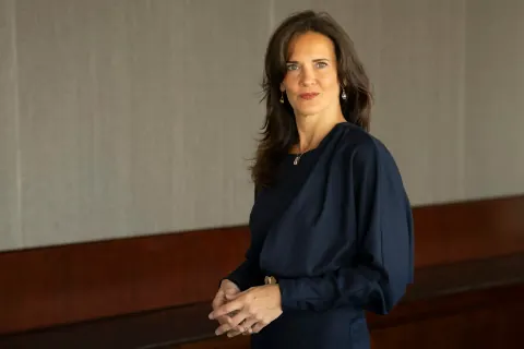 A woman in a navy blouse with her hands clasped beside an office bench.