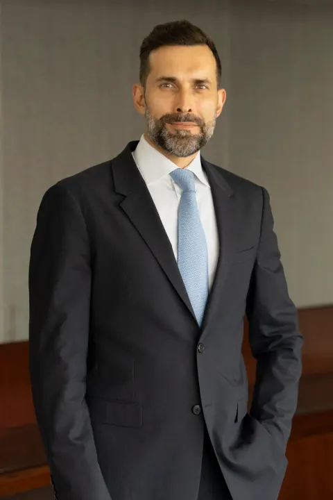 A bearded man in a dark suit and light blue tie.