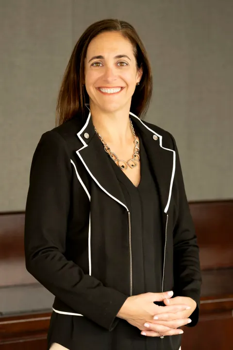 A smiling woman in a black jacket with white piping.