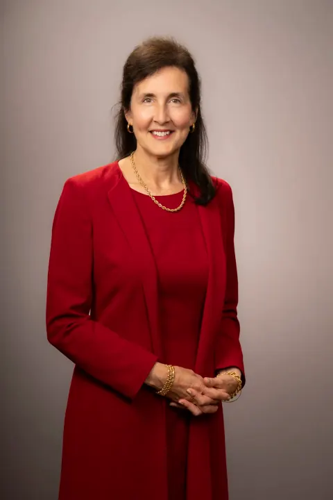 A smiling woman in a red dress with her hands clasped.