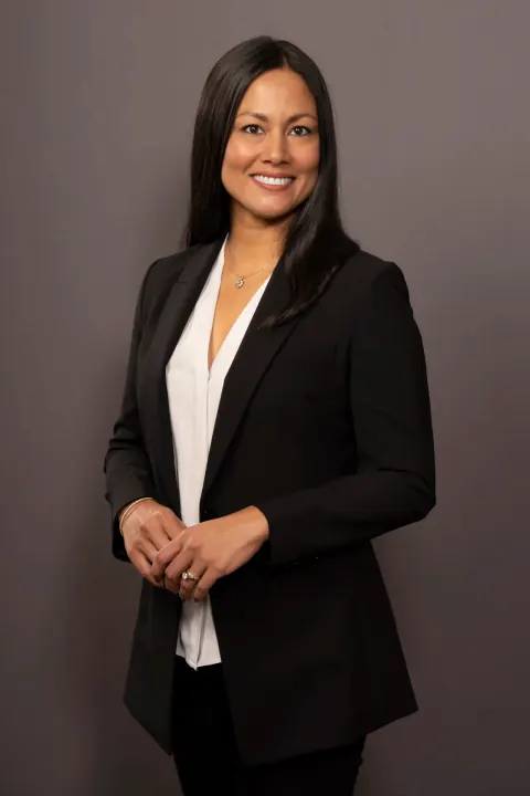 A smiling woman in a black suit and white blouse against a grey backdrop.