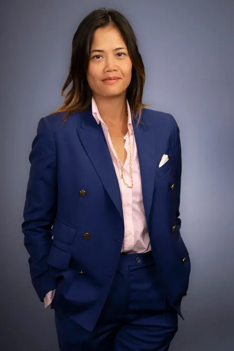 A woman in a blue suit and pink blouse with her hands in her pockets.
