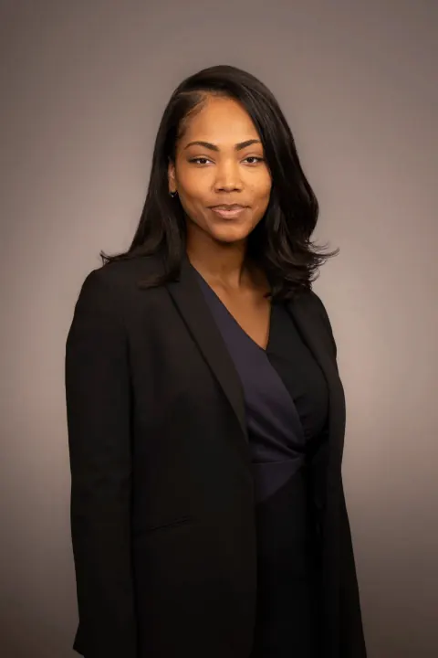 A woman in a black blazer against a grey studio backdrop.