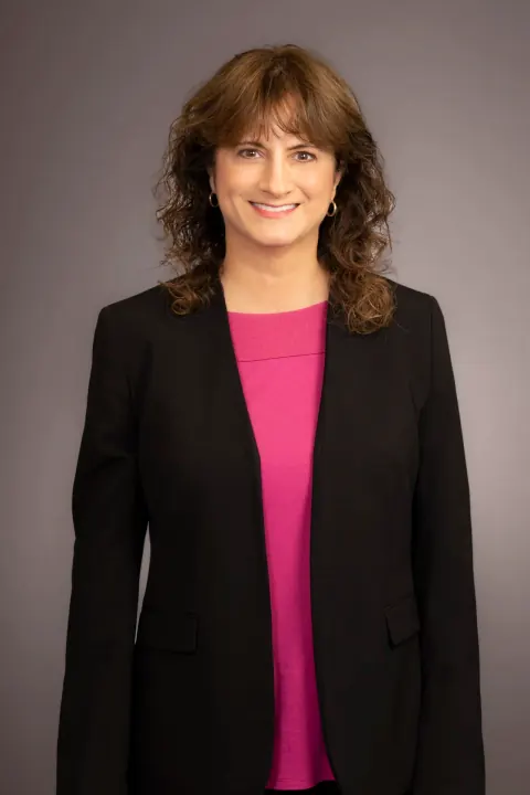 A smiling woman in a black blazer and bright pink top.