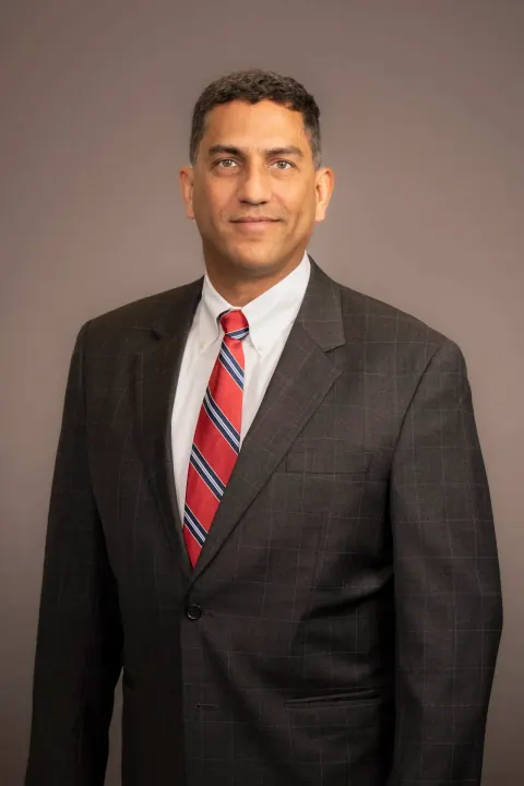 A man in a grey suit and red striped tie against a grey backdrop.