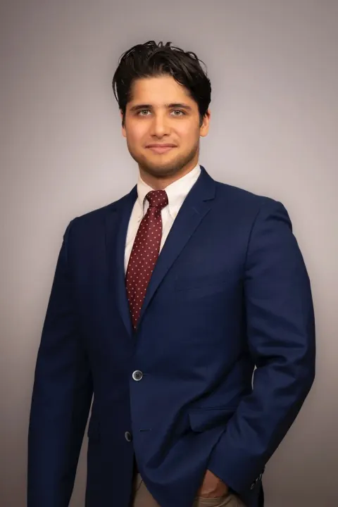 A man in a navy suit and red tie with one hand in his pocket.