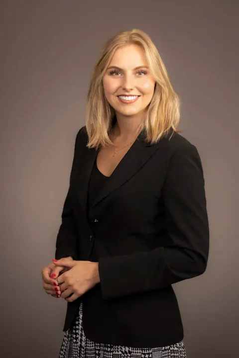 A smiling woman in a black blazer with her hands clasped.