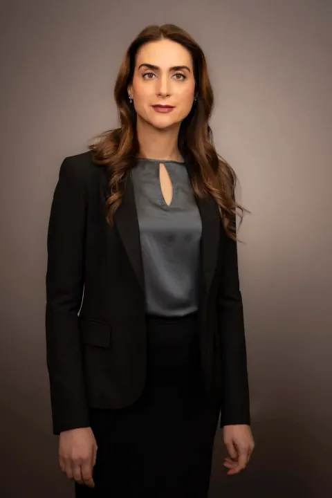 A woman in a black blazer and grey blouse against a studio backdrop.