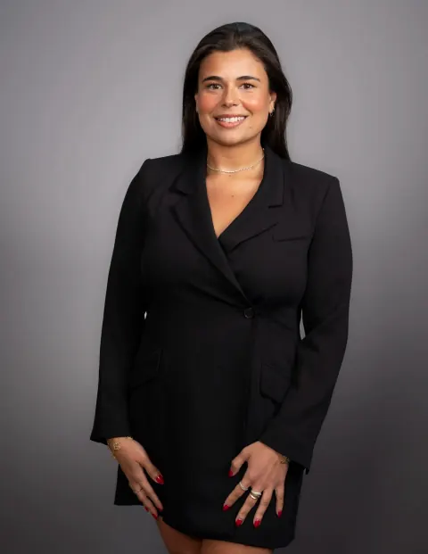 A smiling woman in a black suit with her hands resting in front of her.