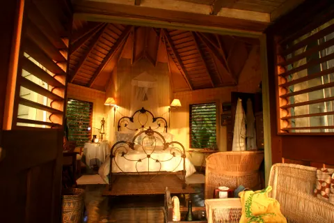 A warmly lit bedroom with a timber ceiling, open shutters and an ornate metal bed.