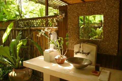 An open-air washbasin surrounded by tropical plants and bamboo walls.