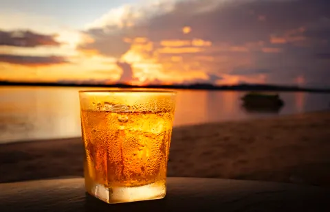 A short glass of amber liquid in front of a beach sunset.