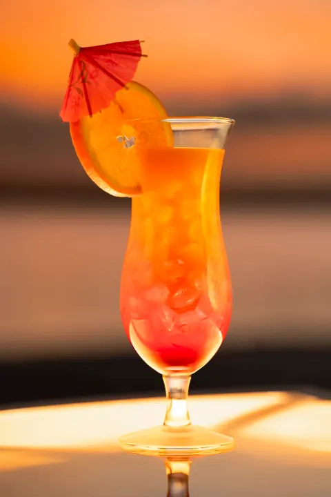 A tall orange cocktail with citrus and a small red umbrella.