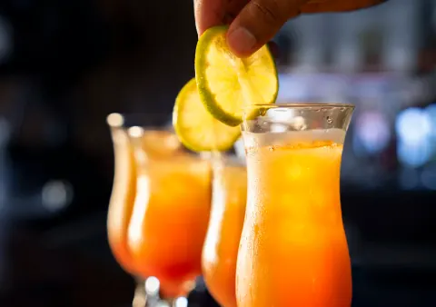 A hand adding a lime slice to an orange cocktail.
