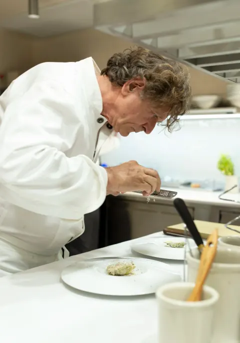 A chef leaning over a plated dish in a restaurant kitchen.