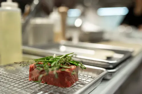A cut of meat topped with herbs on a wire rack.