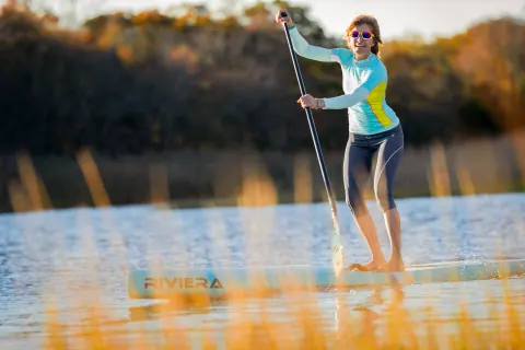 A person standing on a paddleboard against autumn-coloured trees.