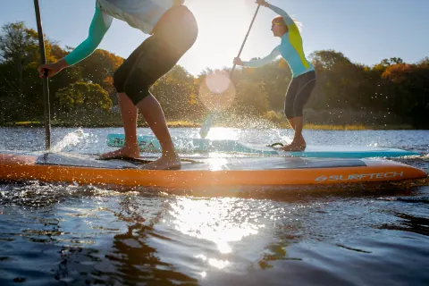 Two paddleboarders crossing sunlit water.