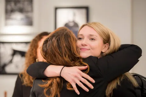 Two women embracing at an event in a room hung with photographs.
