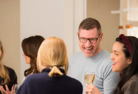 Guests smiling and talking while holding drinks at a gathering.