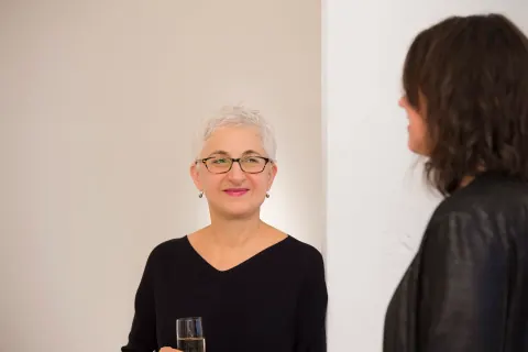 A woman with short grey hair and glasses speaking with a guest.