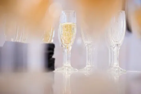 Champagne flutes, one filled, on a reflective surface.