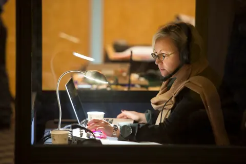 A woman in headphones working at a desk in a broadcast control room.