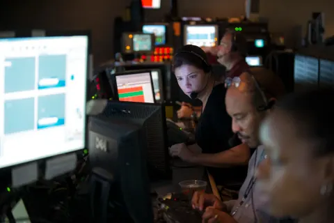 People working together at computer monitors in a dark control room.