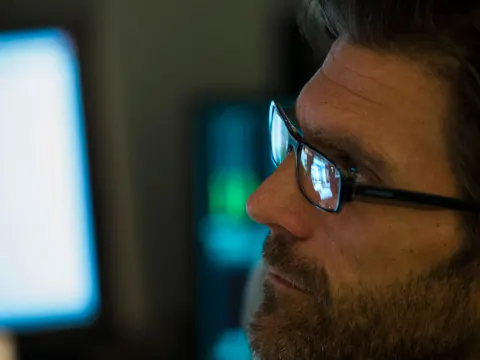 Close-up of a man wearing glasses in a dim control room.
