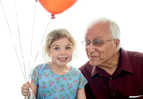 A young girl holding balloons beside a seated man.