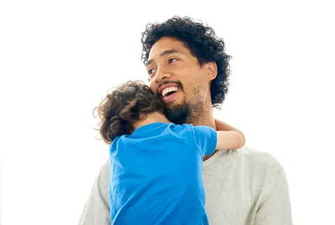 A smiling man carrying a child who has their arms around his neck.