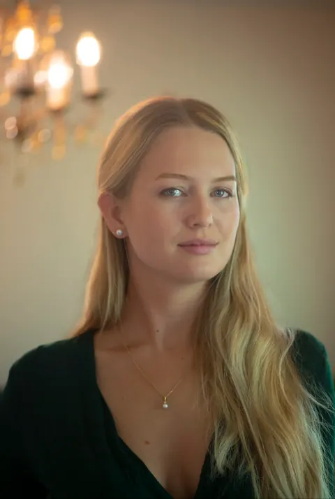 A woman with long blonde hair in a softly lit interior.