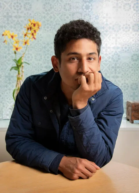 A young man leaning on a table with his hand near his mouth.