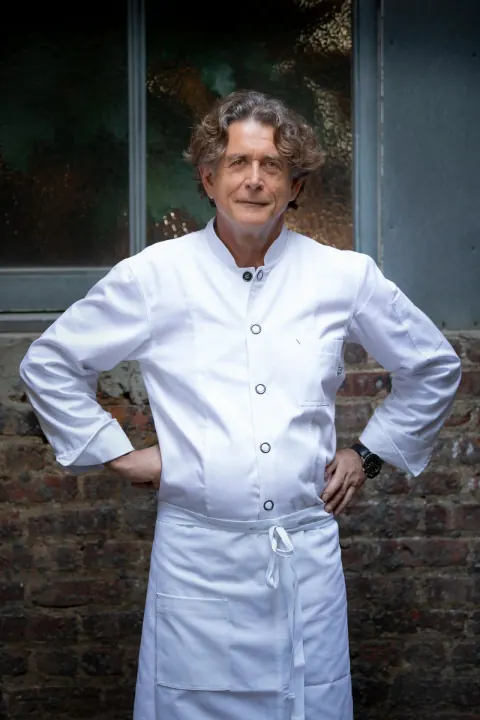 A chef in a white coat standing with hands on hips.
