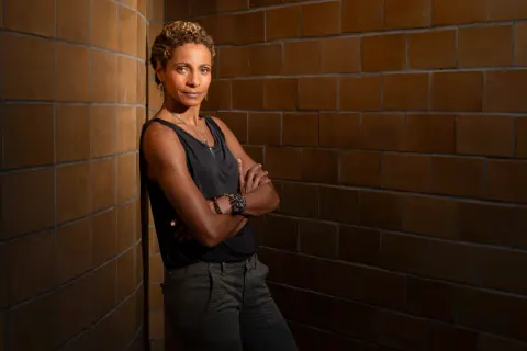 A woman in black with folded arms beside a tiled wall.