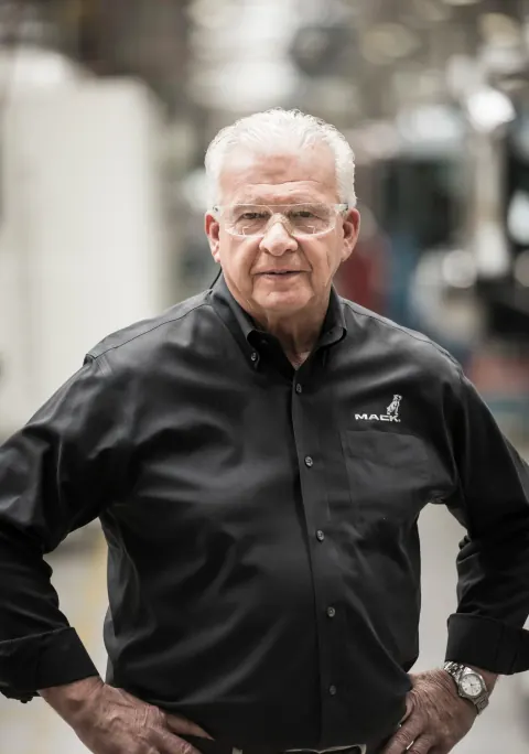 A grey-haired man in glasses and a black polo shirt with hands on hips.