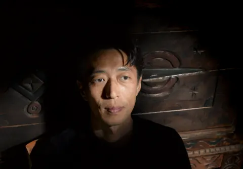 A person in black photographed against a dark wooden background.