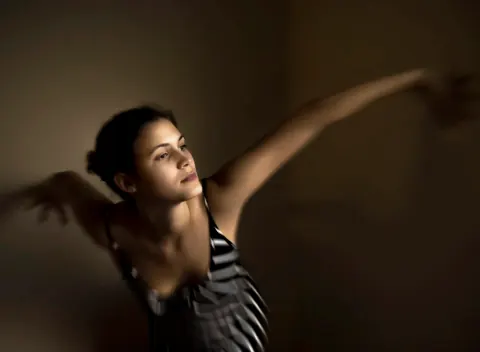 A dancer extending both arms in dramatic side lighting.