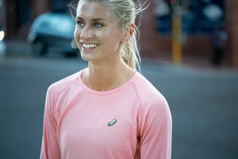 A smiling woman in a pink sports top on a city street.