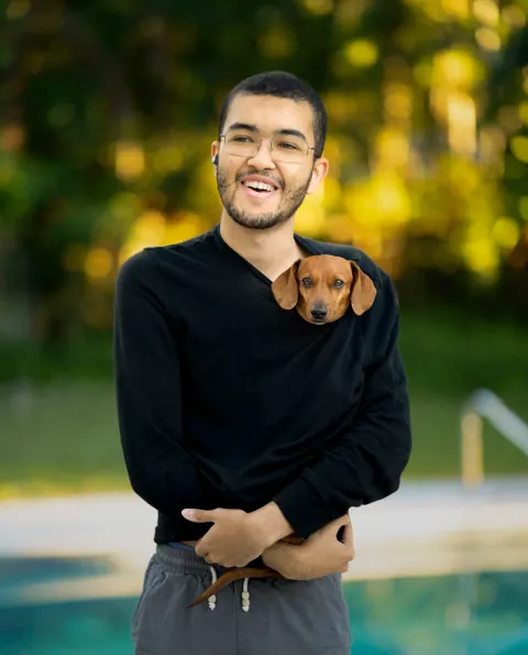 A smiling man holding a small brown dog outdoors.