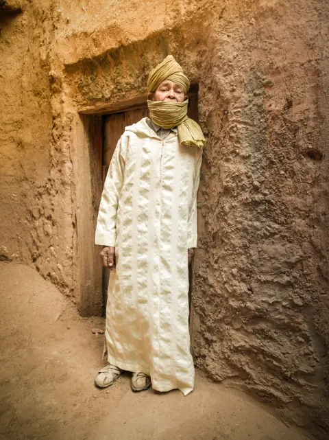 A person in pale patterned clothing standing in a doorway in an earthen wall.