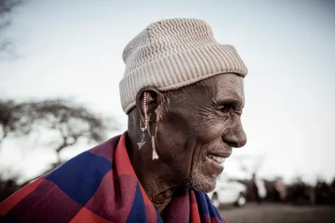 A smiling man in a light knit hat and colourful scarf outdoors.